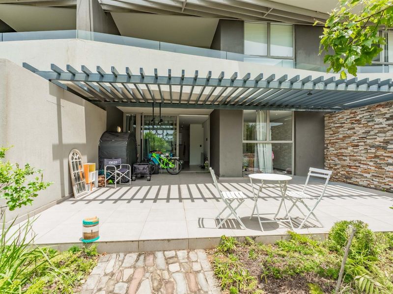 A modern ground floor patio featuring a pergola, glass balustrade, and stone cladding, providing a seamless transition to the interior living space.