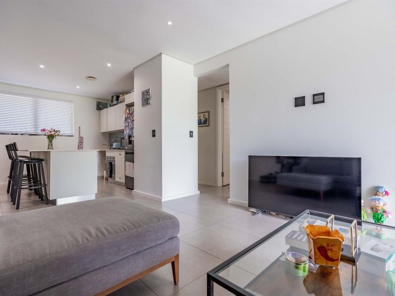 Open-plan living area featuring tiled floors, recessed lighting, and a modern kitchen with a central island and breakfast bar seating.