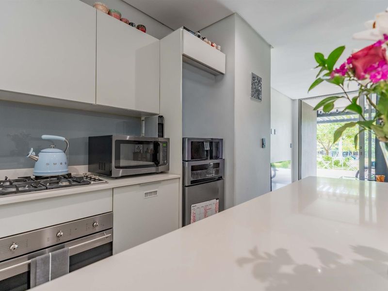 Modern kitchen featuring sleek cabinetry, stone countertops, integrated appliances, and a glass splashback, with a seamless flow to the outdoor patio area.
