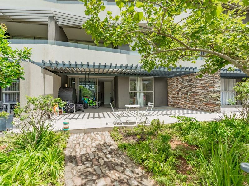 A spacious ground-floor patio featuring a modern pergola, stone feature wall, and glass balustrade, offering seamless indoor-outdoor flow.