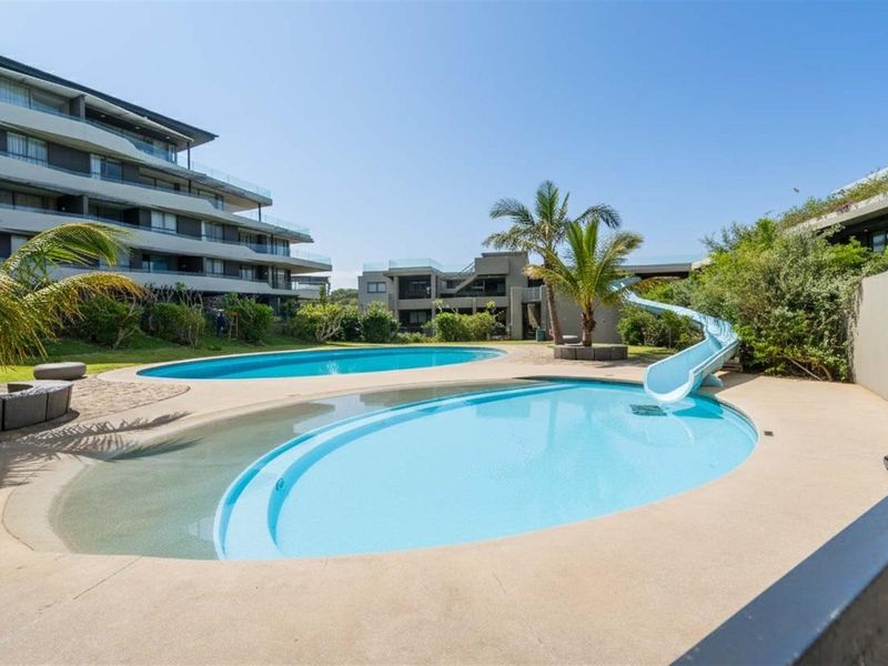 Communal swimming pool area featuring a water slide, paved deck, and landscaped garden surroundings within the apartment complex.