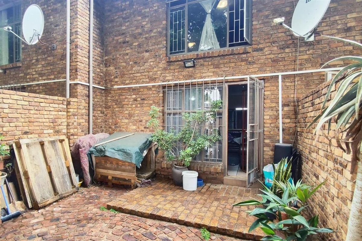 A private rear courtyard featuring exposed brick walls, paved flooring, and secure metal gate access to the apartment interior.