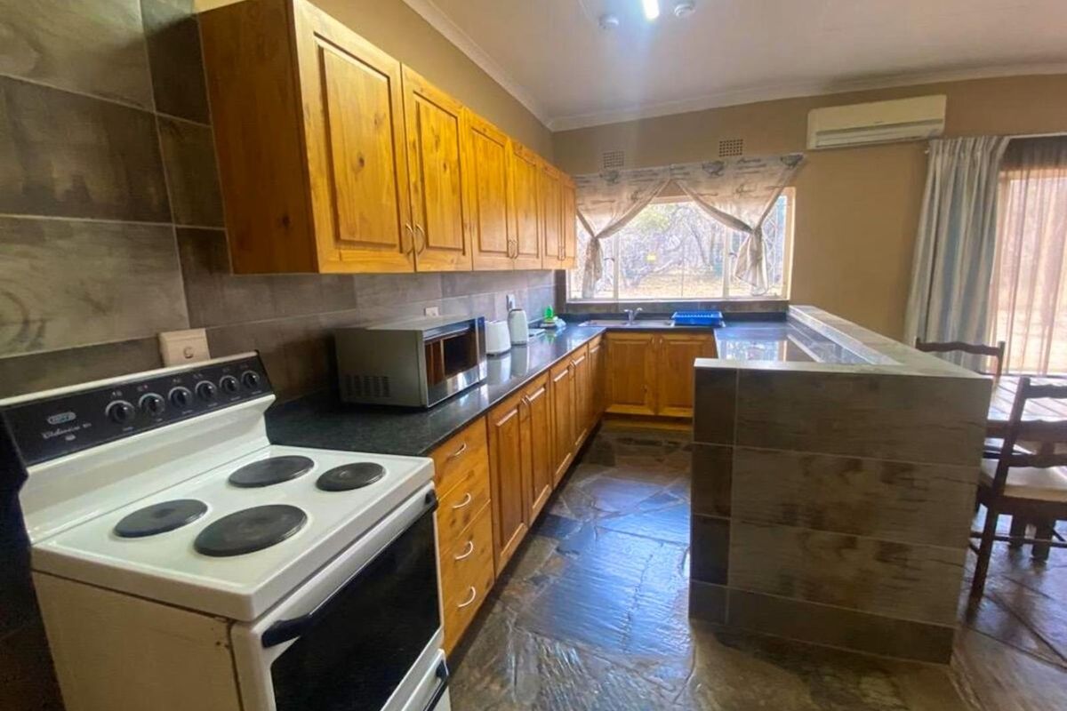 A functional kitchen featuring wooden cabinetry, dark stone countertops, a built-in breakfast bar, and slate flooring, with an integrated stove and air conditioning unit.