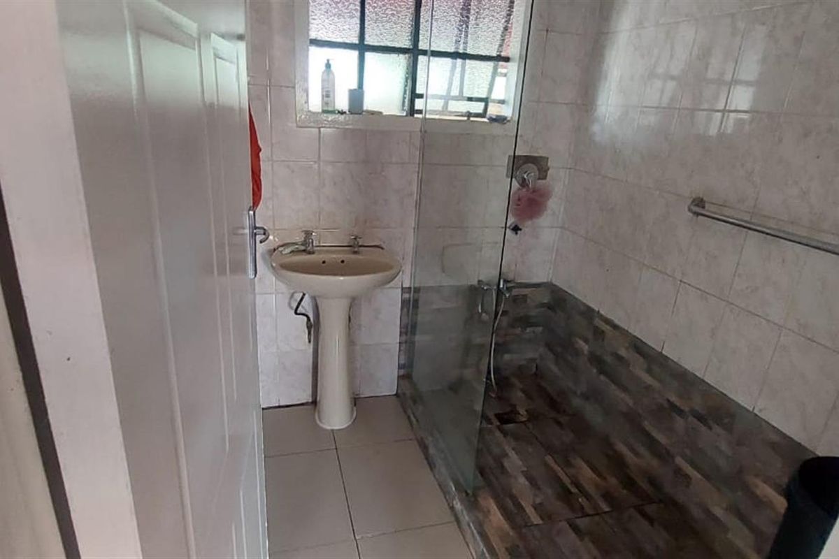 A functional bathroom featuring a pedestal basin, a walk-in shower with a glass screen, and tiled wall finishes.