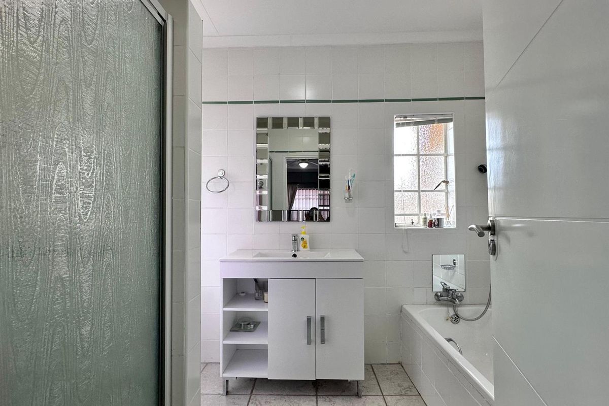 A functional bathroom featuring a vanity cabinet, bathtub, and separate shower enclosure with white wall tiling and tiled flooring.