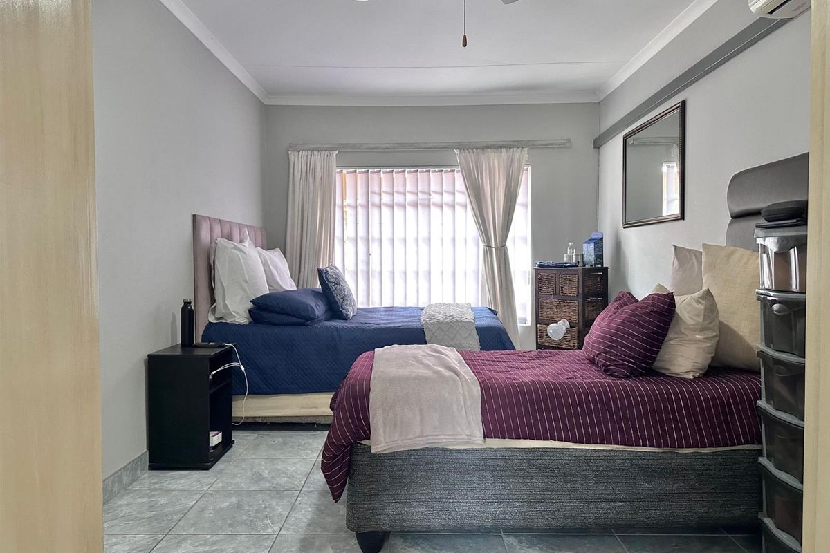 A bedroom featuring tiled flooring, a ceiling fan, and an air conditioning unit, providing a functional space with neutral wall finishes.