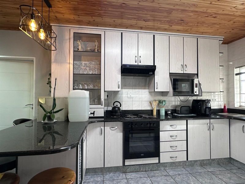 A well-maintained kitchen featuring light wood-grain cabinetry, dark granite countertops, integrated appliances, and a distinctive timber-paneled ceiling.