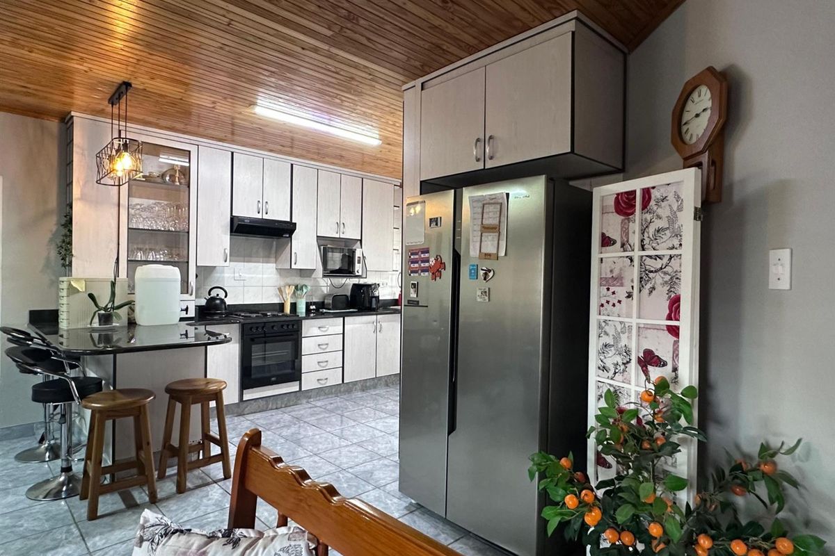 A functional kitchen featuring built-in cabinetry, granite countertops, integrated appliances, tiled flooring, and a distinctive timber-clad ceiling.