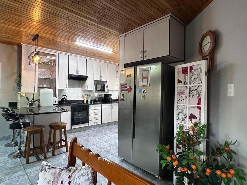A functional kitchen featuring built-in cabinetry, granite countertops, integrated appliances, tiled flooring, and a distinctive timber-clad ceiling.