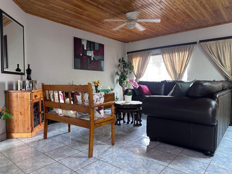 A living room featuring a warm timber tongue and groove ceiling, ceiling fan, and tiled flooring, offering a comfortable and functional living space.