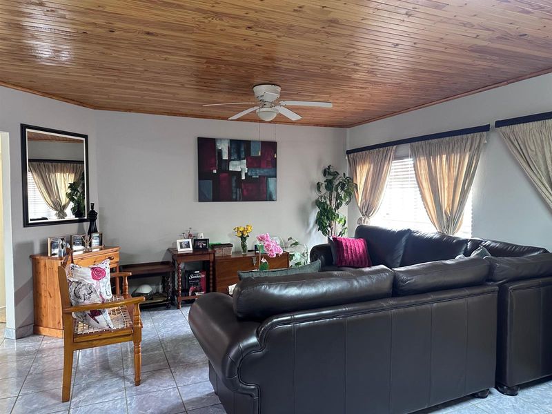 A comfortable living room featuring a warm timber tongue and groove ceiling, ceiling fan, and neutral tiled flooring, offering a cozy and inviting atmosphere.