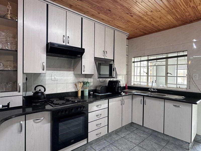 Functional kitchen featuring light wood-grain cabinetry, black granite countertops, built-in oven and hob, and a distinctive timber-paneled ceiling.