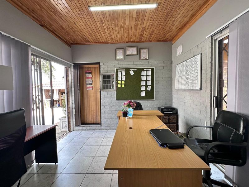 A functional home office featuring exposed timber ceilings, painted brick walls, and ceramic tiled flooring with direct access to the outdoor area.