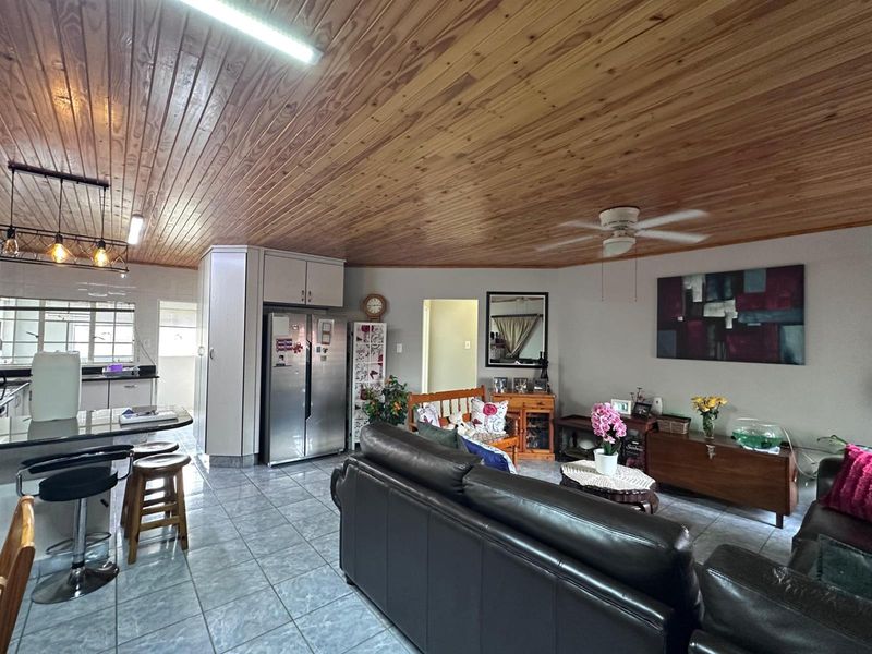 Open plan living and kitchen area featuring tiled flooring, a timber tongue and groove ceiling, and a functional kitchen layout with island seating.