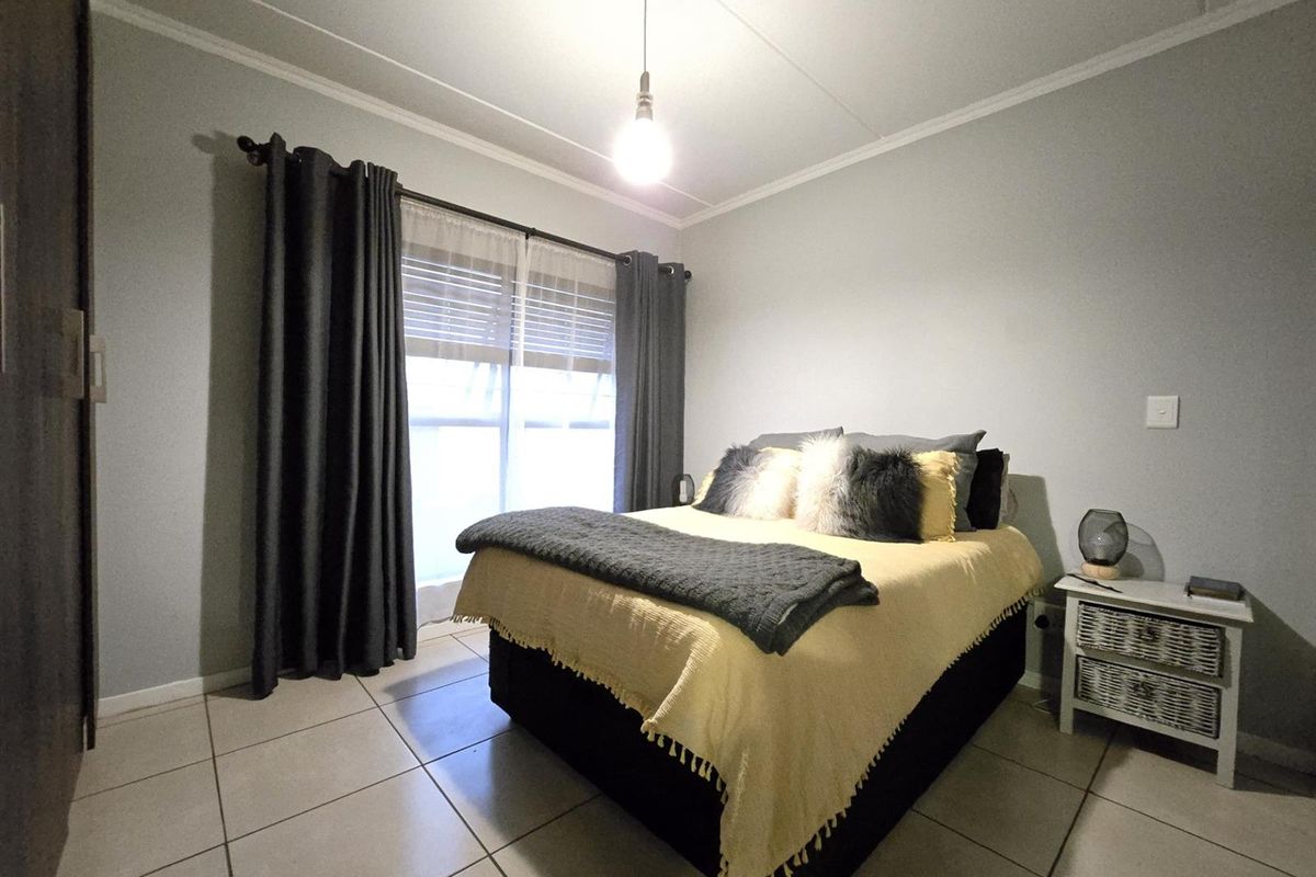 A well-lit bedroom featuring neutral tiled flooring, a built-in wardrobe, and large windows with curtains, providing a comfortable and functional living space.