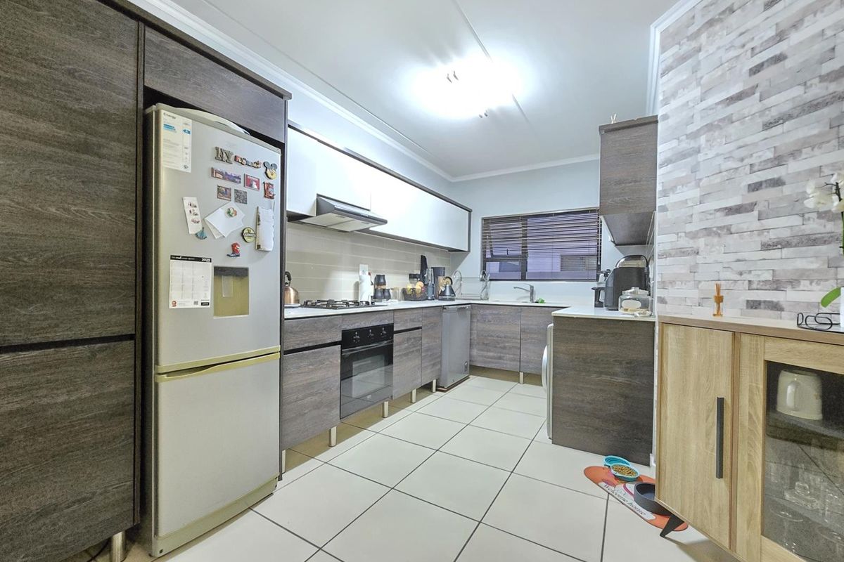 A functional kitchen featuring dark wood-grain cabinetry, a built-in oven, gas hob, extractor fan, and tiled flooring with a stone-cladding feature wall.