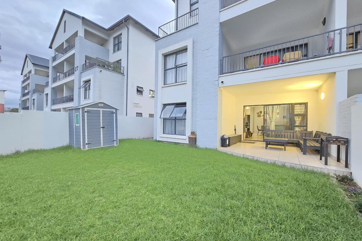 Ground floor apartment featuring a private garden, a covered patio area, and a storage shed, set within a modern residential complex.