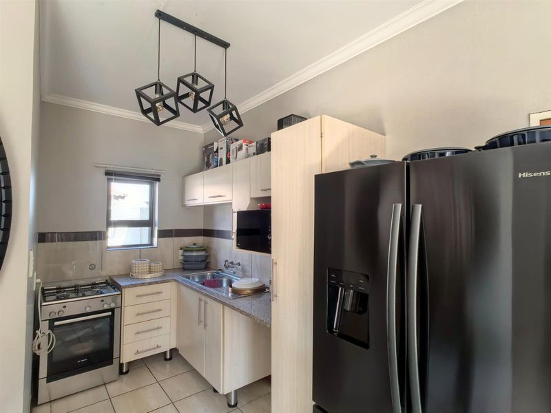 A functional kitchen featuring light-toned cabinetry, granite countertops, a gas stove with oven, and tiled flooring, complemented by modern pendant lighting.