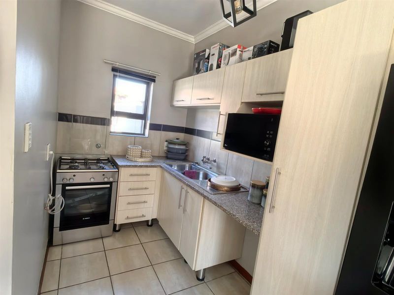 Compact kitchen featuring light wood-finish cabinetry, granite countertops, a gas stove with oven, and tiled flooring.