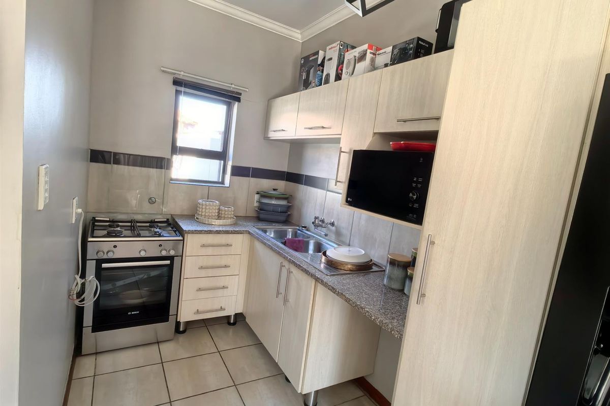 Compact kitchen featuring light wood-finish cabinetry, granite countertops, a gas stove with oven, and tiled flooring.
