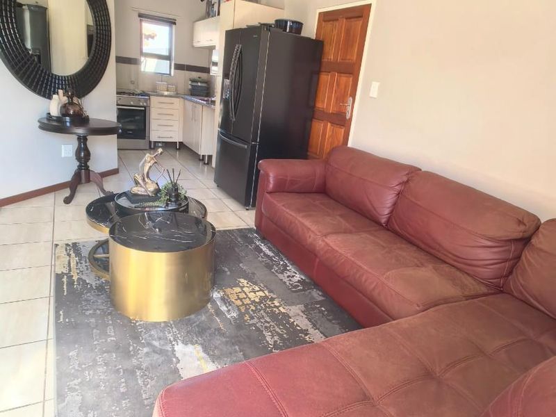 Open-plan living area featuring tiled flooring and a compact kitchen with built-in cabinetry, oven, and hob, seamlessly connected to the lounge space.