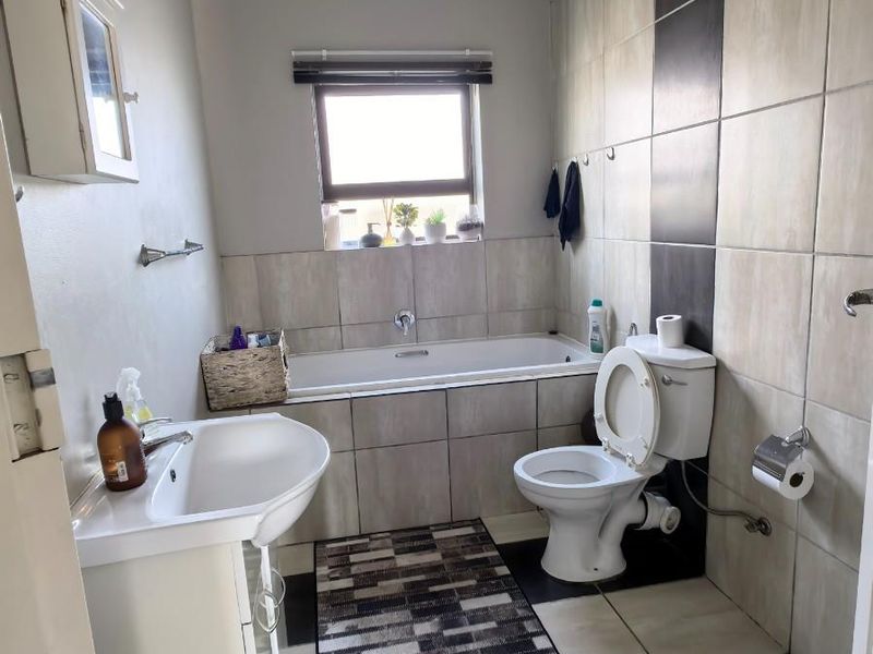 A functional bathroom featuring a bathtub, pedestal sink, and toilet with neutral wall and floor tiling.