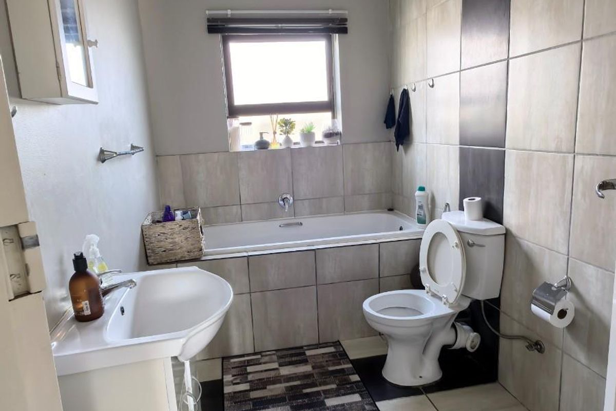 A functional bathroom featuring a bathtub, pedestal sink, and toilet with neutral wall and floor tiling.