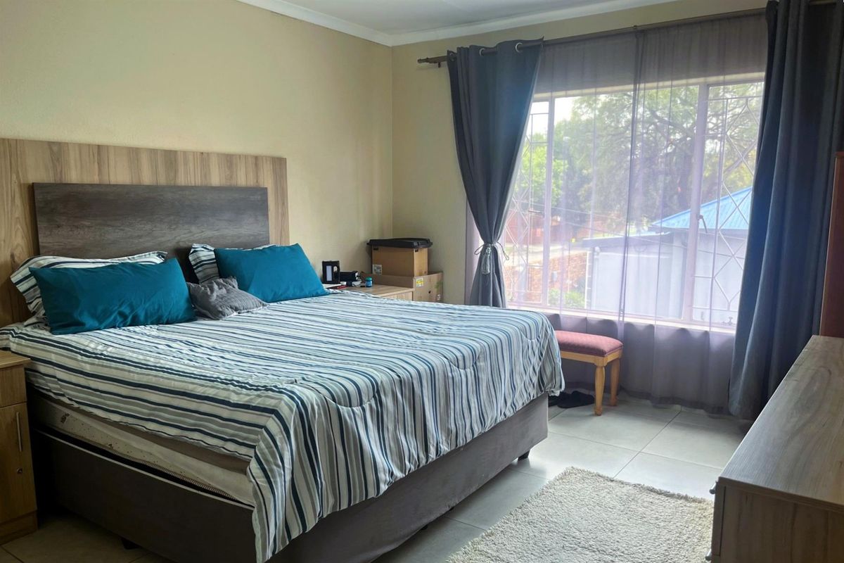 A well-lit bedroom featuring tiled flooring, a large window with security bars, and neutral wall finishes.