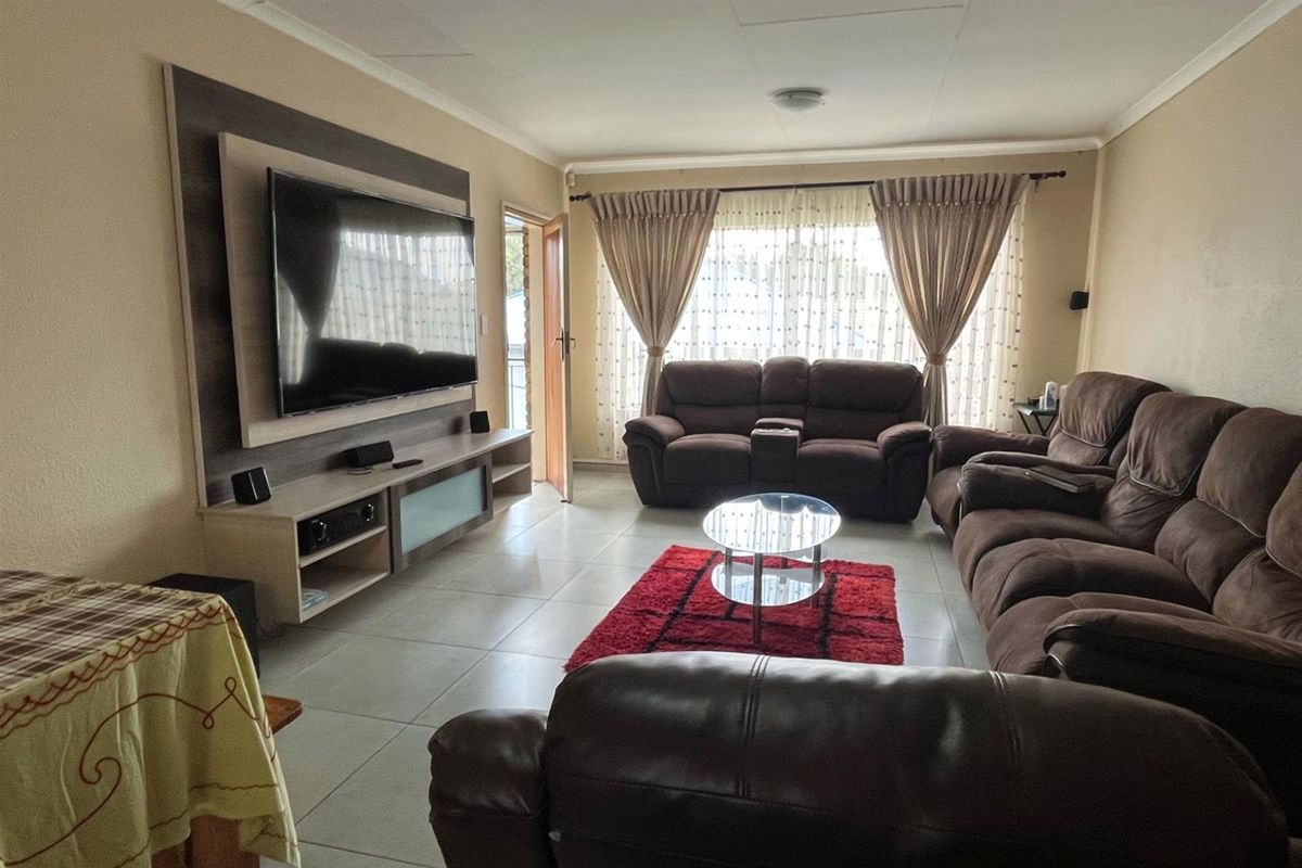 A comfortable living room featuring tiled flooring, a built-in media wall unit, and large windows allowing for natural light.