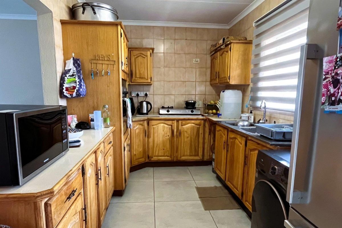 A functional kitchen featuring wooden cabinetry, tiled splashbacks, a double sink, and integrated space for laundry appliances.
