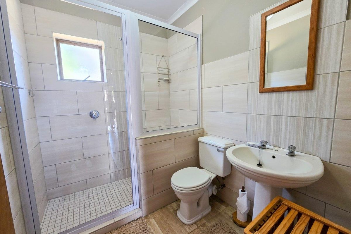 A clean, functional bathroom featuring a glass-enclosed shower, pedestal basin, and toilet with neutral wall and floor tiling.