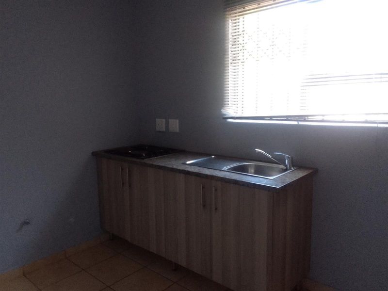 A compact kitchen area featuring built-in cabinetry, a stainless steel sink with mixer tap, and a built-in hob, finished with tiled flooring.