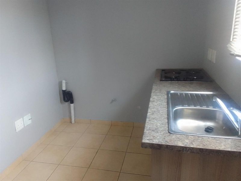 A compact kitchen area featuring a built-in sink, laminate countertop, and gas hob, with tiled flooring and plumbing connections for appliances.