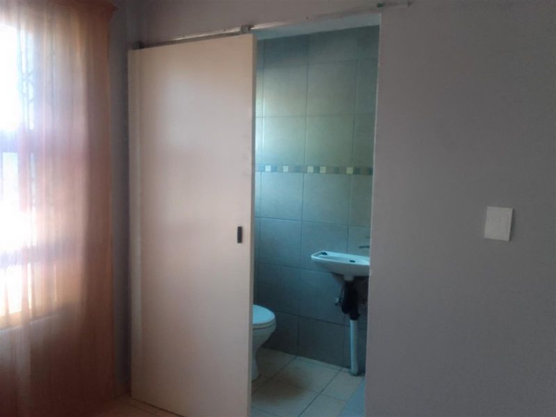 A compact bathroom featuring a wall-mounted basin, toilet, and tiled walls, accessed via a sliding door.