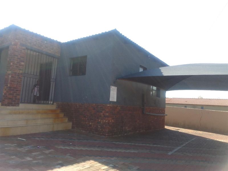 Front exterior view of the cottage featuring a brick and rendered facade, paved driveway, and a shade cloth carport.