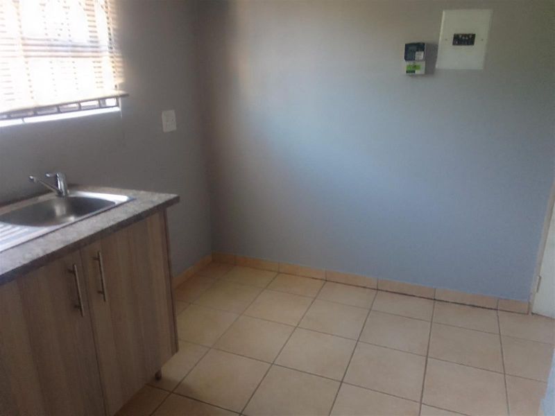 A functional laundry area featuring a stainless steel sink, base cabinetry with laminate countertop, and neutral ceramic floor tiles.