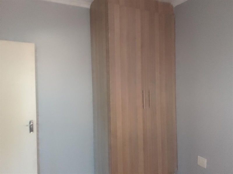 A simple bedroom interior featuring a built-in wooden wardrobe and a standard internal door.