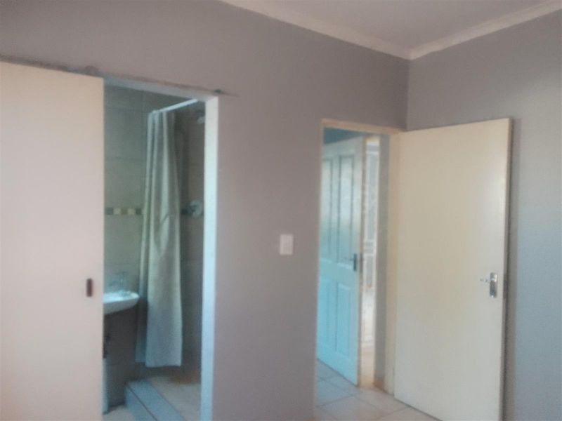 A neutral bedroom interior featuring tiled flooring, coving, and direct access to an en-suite bathroom and hallway.