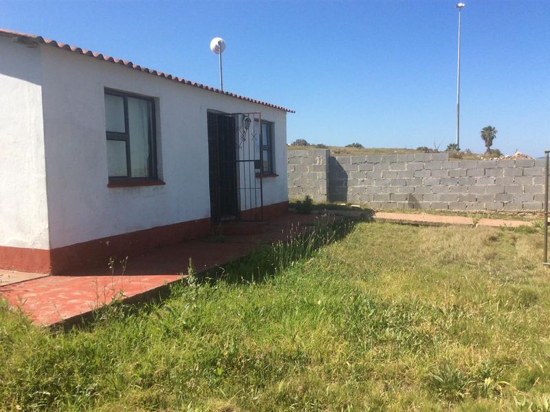 Rear view of the property featuring a small concrete patio, security gate, and an unfinished concrete block boundary wall with an overgrown lawn.