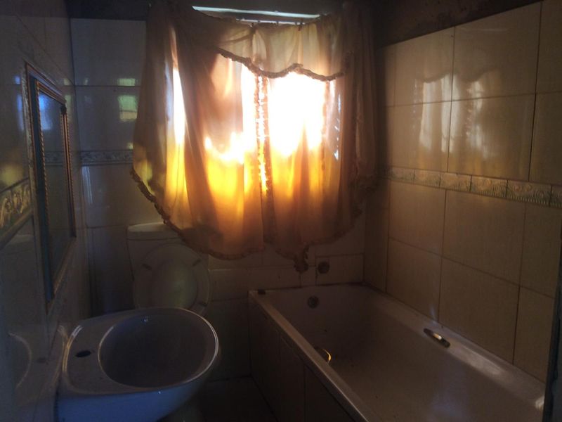 A dated bathroom featuring a bathtub, toilet, and pedestal basin with wall tiling, requiring modernization and improved lighting.