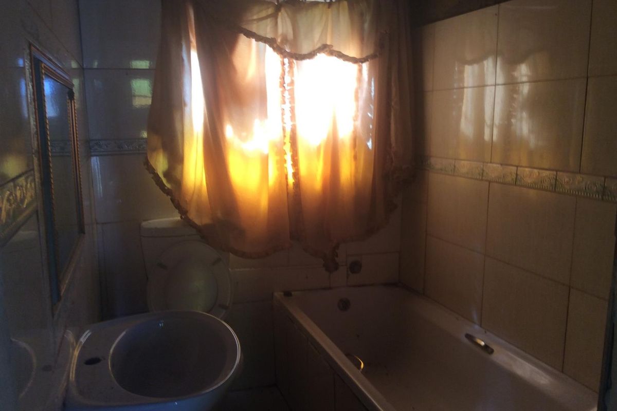 A dated bathroom featuring a bathtub, toilet, and pedestal basin with wall tiling, requiring modernization and improved lighting.