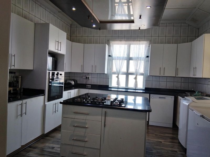 A functional kitchen featuring white cabinetry, black granite countertops, a central island with a gas hob, and integrated oven, complemented by recessed ceiling lighting.