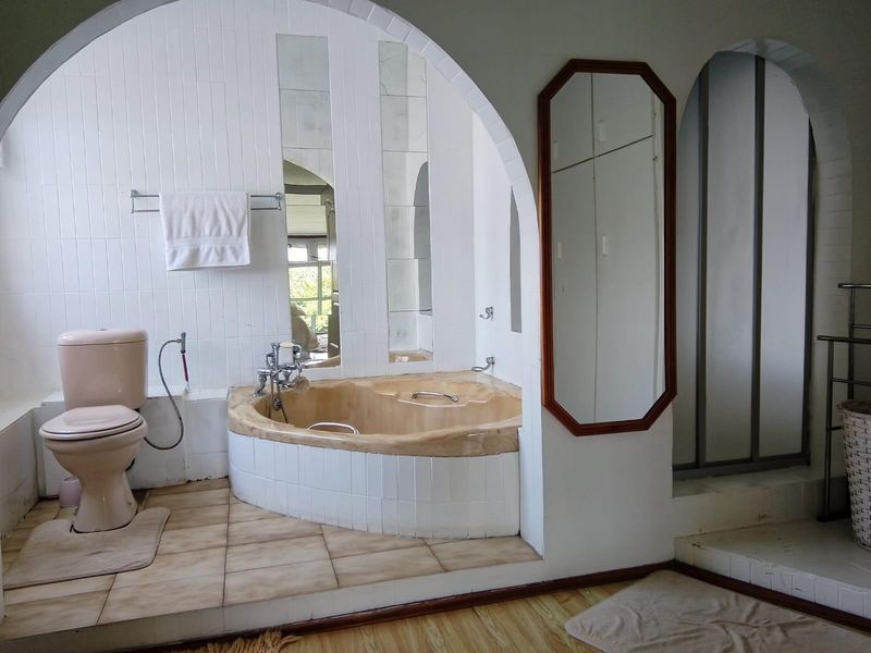 A dated bathroom featuring a built-in bathtub set within an arched alcove, tiled flooring, and a separate toilet area.