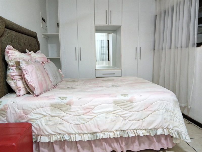 A well-maintained bedroom featuring floor-to-ceiling built-in wardrobes with an integrated vanity mirror and neutral tiled flooring.
