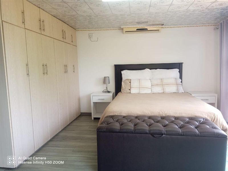 A bedroom featuring extensive built-in cupboards, laminate flooring, and a wall-mounted air conditioning unit.