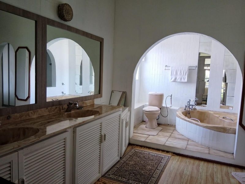Spacious bathroom featuring a double vanity with stone countertop, a sunken bathtub, and a separate toilet area, all framed by a distinctive architectural archway.