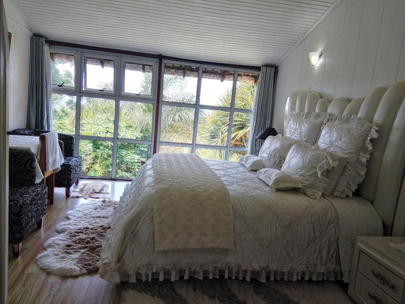 A spacious bedroom featuring large windows that provide ample natural light and views of the surrounding greenery, complemented by laminate flooring.