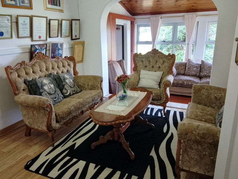 A living room featuring timber-look laminate flooring, a timber-lined ceiling, and an archway leading to an adjacent seating area with large windows.