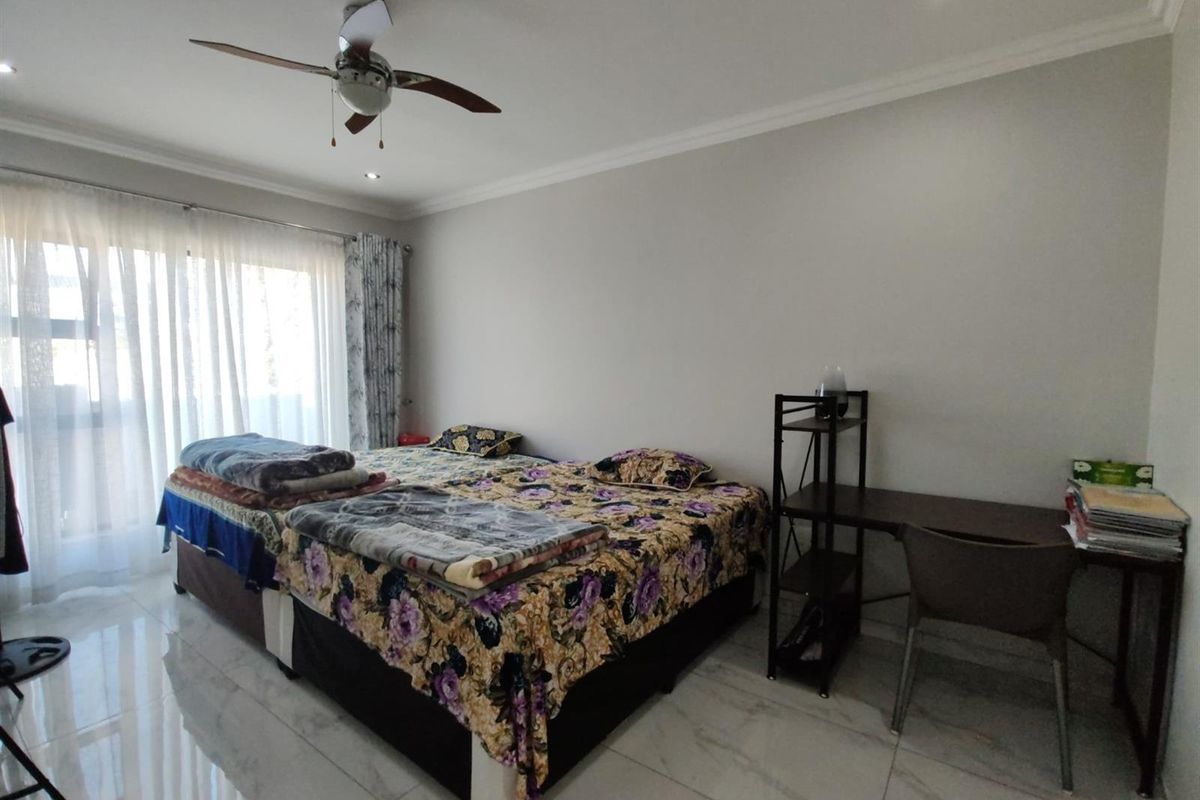 A well-lit bedroom featuring polished tile flooring, a ceiling fan, and large windows with sheer curtains, providing a bright and comfortable living space.