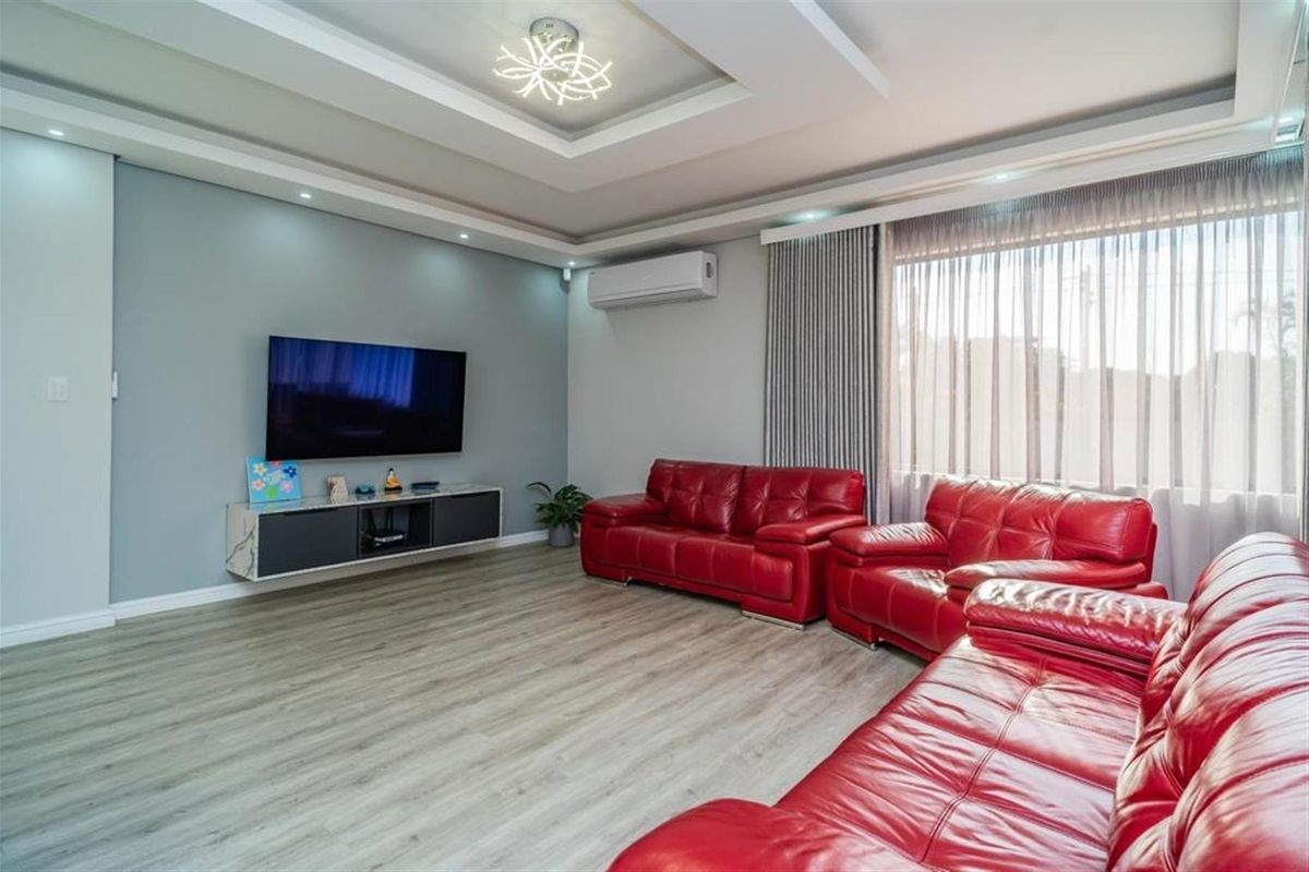 A modern living room featuring a tray ceiling with recessed lighting, wood-look flooring, and a wall-mounted air conditioning unit.